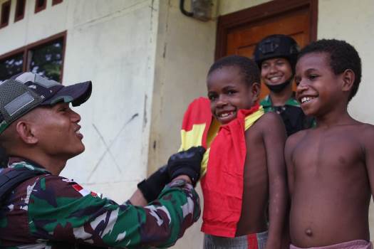 Prajurit Satgas Pamtas sedang mengenapakan pakaian kepada salah seorang anak – Surya Papua/IST