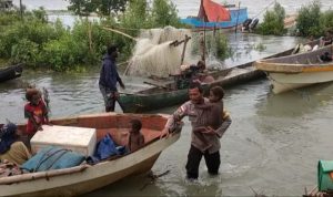 Salah seorang anggota Polsek Kimaam sedang menggendong seorang bocah untuk dinaikkan ke atas speedboat – Surya Papua/IST
