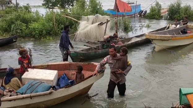 Salah seorang anggota Polsek Kimaam sedang menggendong seorang bocah untuk dinaikkan ke atas speedboat – Surya Papua/IST