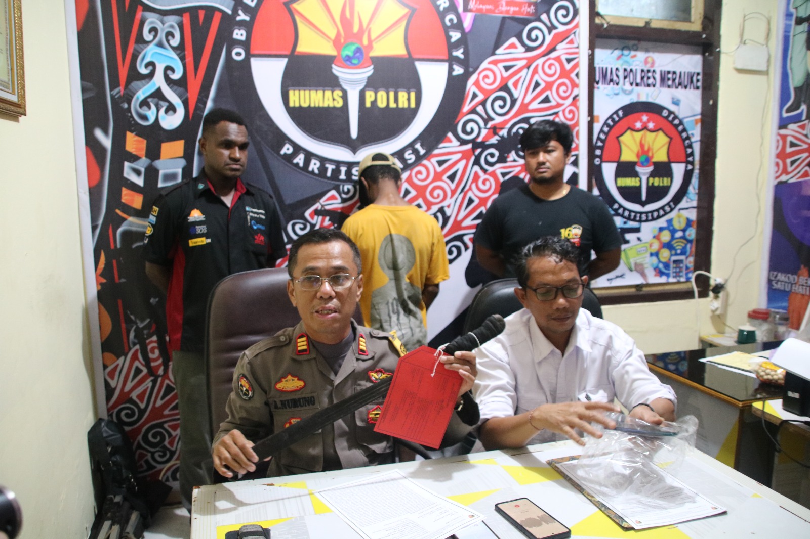 Kasi Humas Polres Merauke, AKP Ahmad Nurung didamoingi KBO Satreskrim Polres setempat, Ipda Sewang sedang menunjik barang bukti parang serta handphone korban yang diamankan – Surya Papua/Frans Kobun