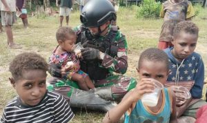 Salah seorang prajurit Satgas sedang membantu memberikan susu ke anak yang digendongnya – Surya Papua/IST