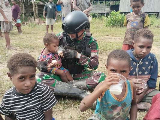 Salah seorang prajurit Satgas sedang membantu memberikan susu ke anak yang digendongnya – Surya Papua/IST