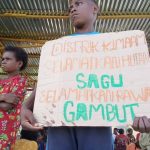 Seorang anak di Kampung Kiworo, Distrik Kimaam sedang memegang sehelai kertas dengan tulisan penolakan PSN saat aksi di Lapangan Maskura-Kimaam – Surya Papua/Frans Kobun