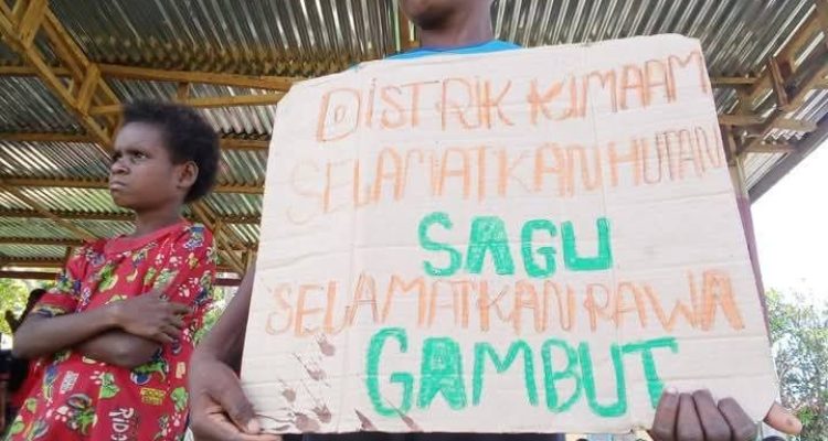 Seorang anak di Kampung Kiworo, Distrik Kimaam sedang memegang sehelai kertas dengan tulisan penolakan PSN saat aksi di Lapangan Maskura-Kimaam – Surya Papua/Frans Kobun